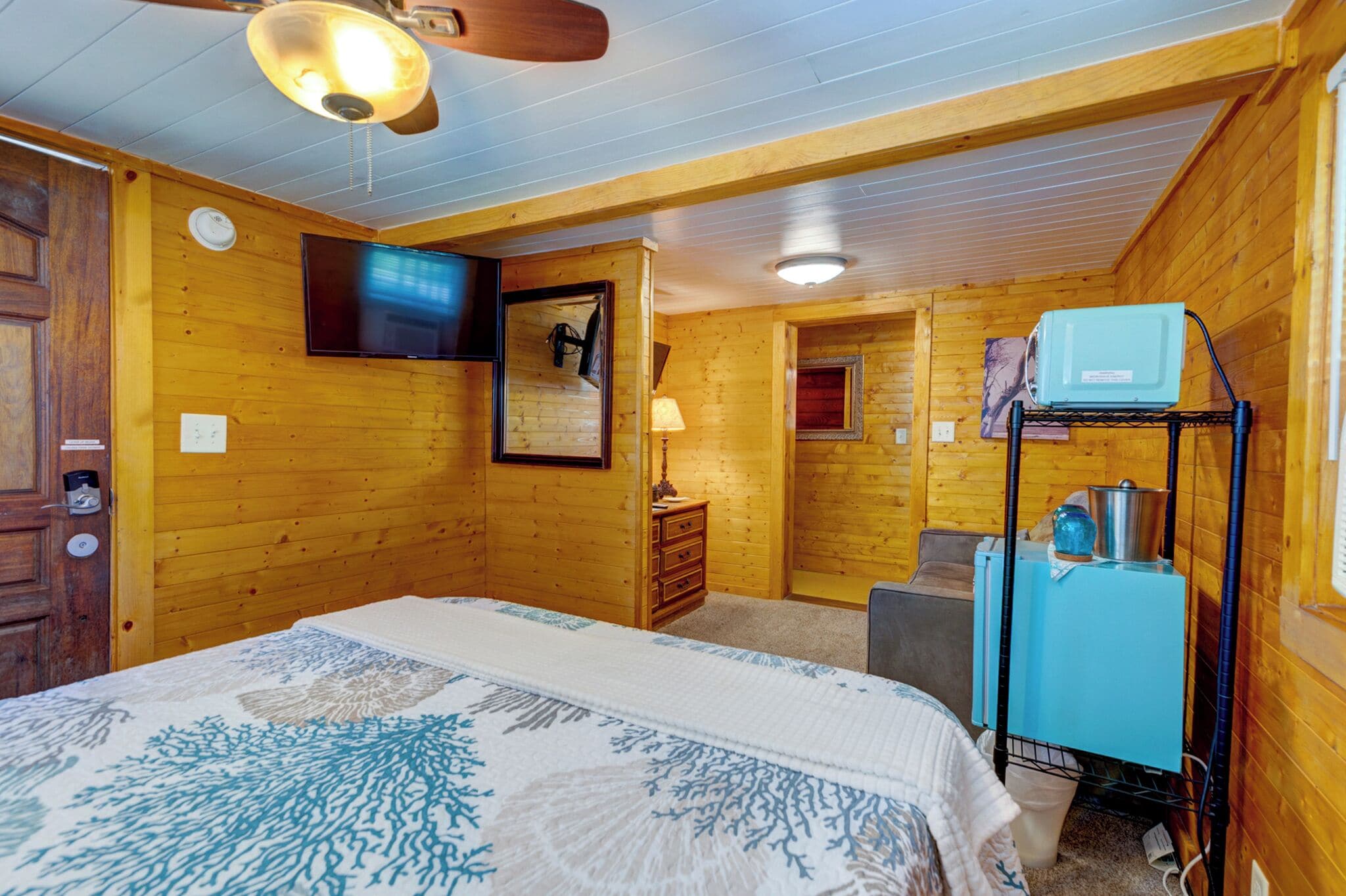 Ein Schlafzimmer mit Holzvertäfelung, einem Bett, einem Fernseher, einem Schminktisch und einer Küchenzeile.