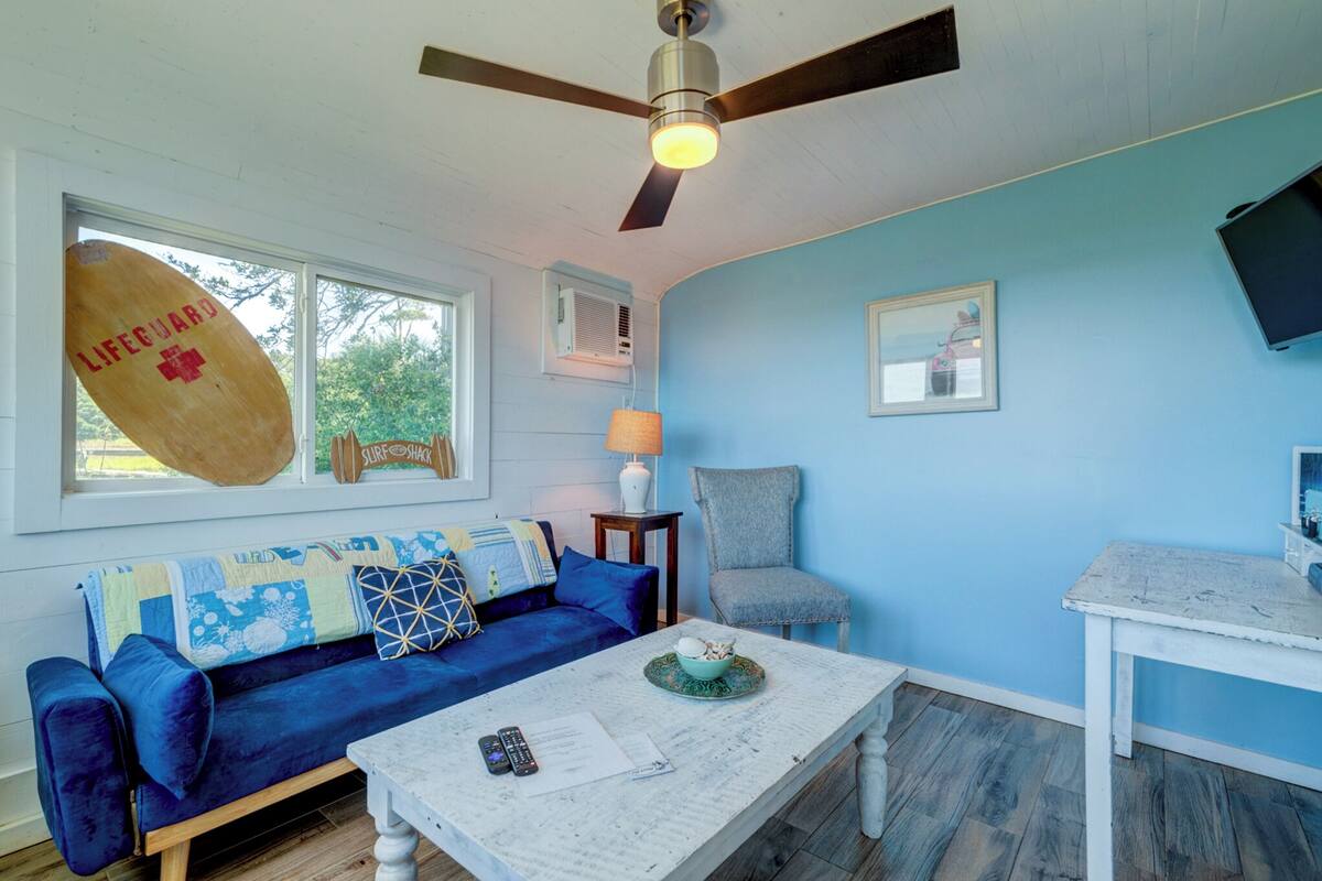 A living room with a blue sofa, a white coffee table, a ceiling fan, and a TV on a white table.