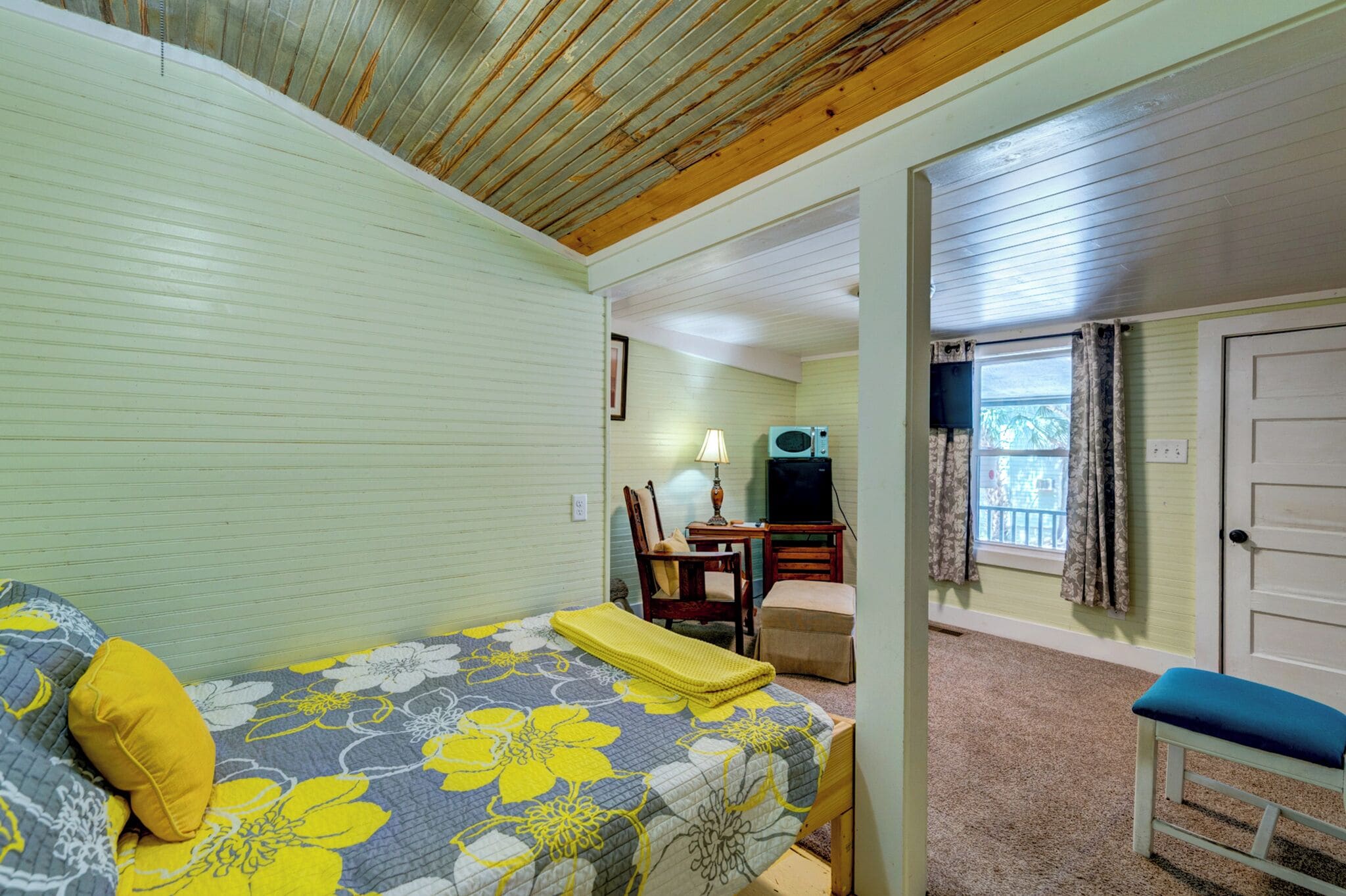 A bedroom with a bed, a desk, a chair, and a window with curtains.