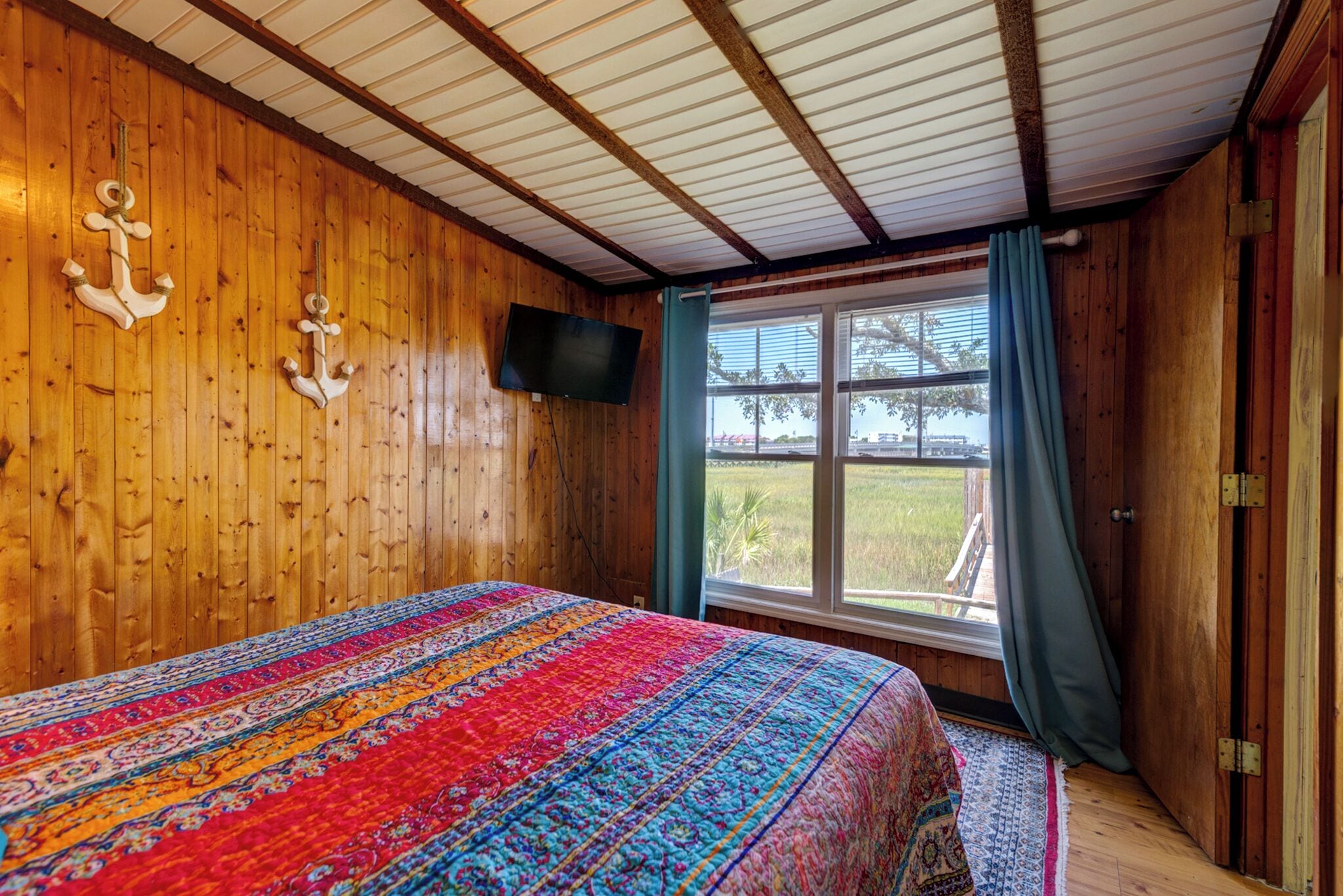 Una habitación de madera con una cama, un televisor y una ventana con cortinas.