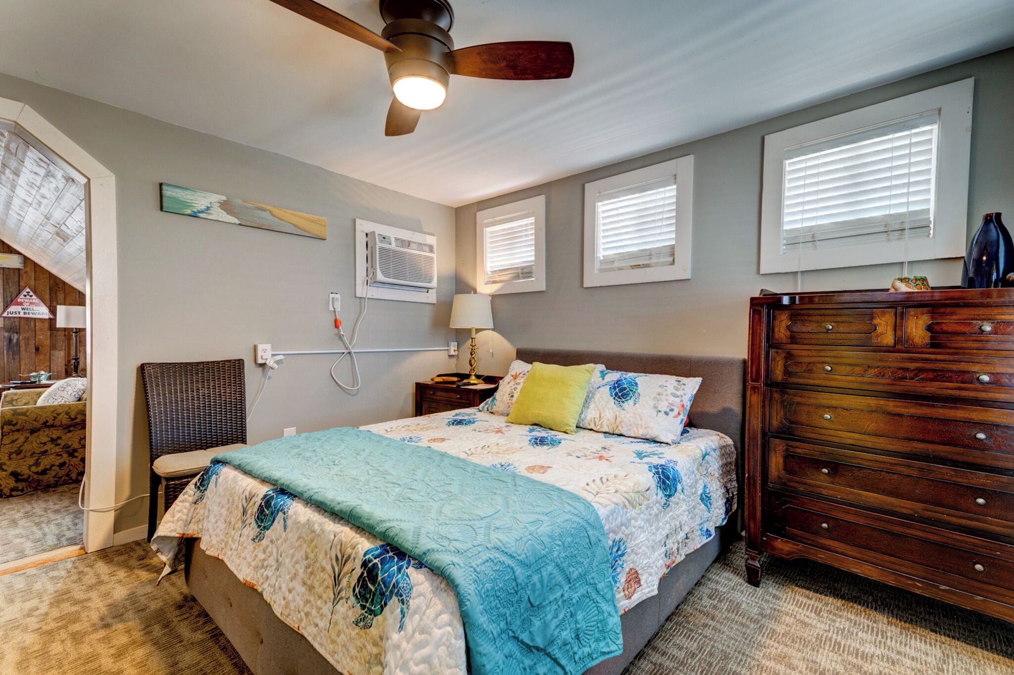 A bedroom with a bed, a dresser, a chair, a ceiling fan, and a window with blinds.