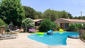 Una piscina con anillos flotantes, una terraza de madera y un pequeño edificio con techo de tejas.
