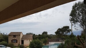 Vista desde un balcón sobre una piscina, una casa de piedra y un coche aparcado en la entrada.