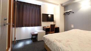 Una habitación de hotel con cama, escritorio, silla, televisor y armario.