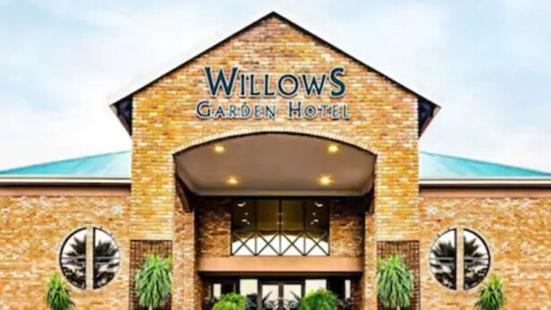 Exterior do Hotel Willows Garden, com fachada de tijolos, janelas amplas e plantas em vasos na entrada.