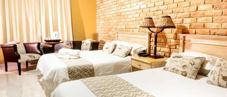 A hotel room with two beds, a brick wall, a desk with a lamp, and a chair.