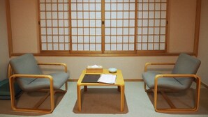 Una habitación tradicional japonesa con suelo de tatami, dos esteras de tatami, una mesa de madera baja con papeles y un cuenco, y dos sillas de tatami.