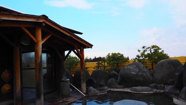 Una estructura de madera con techo, una piscina de piedra y grandes rocas a su alrededor.