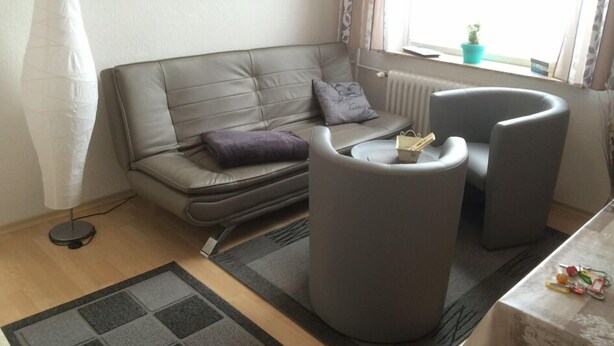 En moderne stue med en grå sofa, en lille lænestol, en gulvlampe og havudsigt fra vinduet.