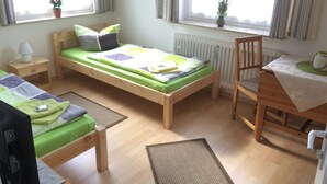 Et lille, godt oplyst værelse med en enkelt seng, en stol, et bord og en radiator.