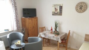 En stue med fjernsyn, spisebord med stole, sofa og en radiator.