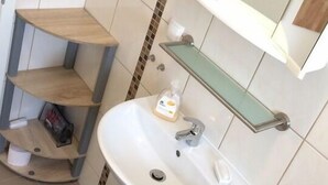 Et badeværelse med en hvid vask, et spejl over og en hylde med toiletartikler.