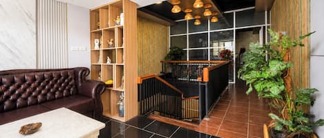 Un interior moderno con un sofá de cuero, una mesa blanca, una estantería de madera y una escalera que baja a un nivel inferior.
