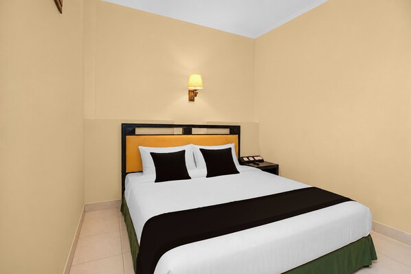 A neatly made bed with a headboard, a bedside table with a lamp, and a wall-mounted light fixture. - Collection O 637 Yasmin Hotel (Makassar)