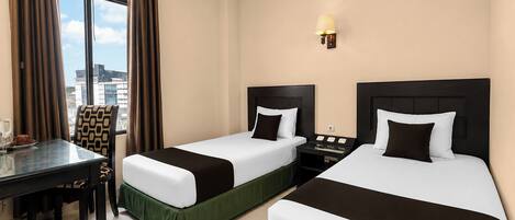 A hotel room with two beds, a desk, and a window with curtains.