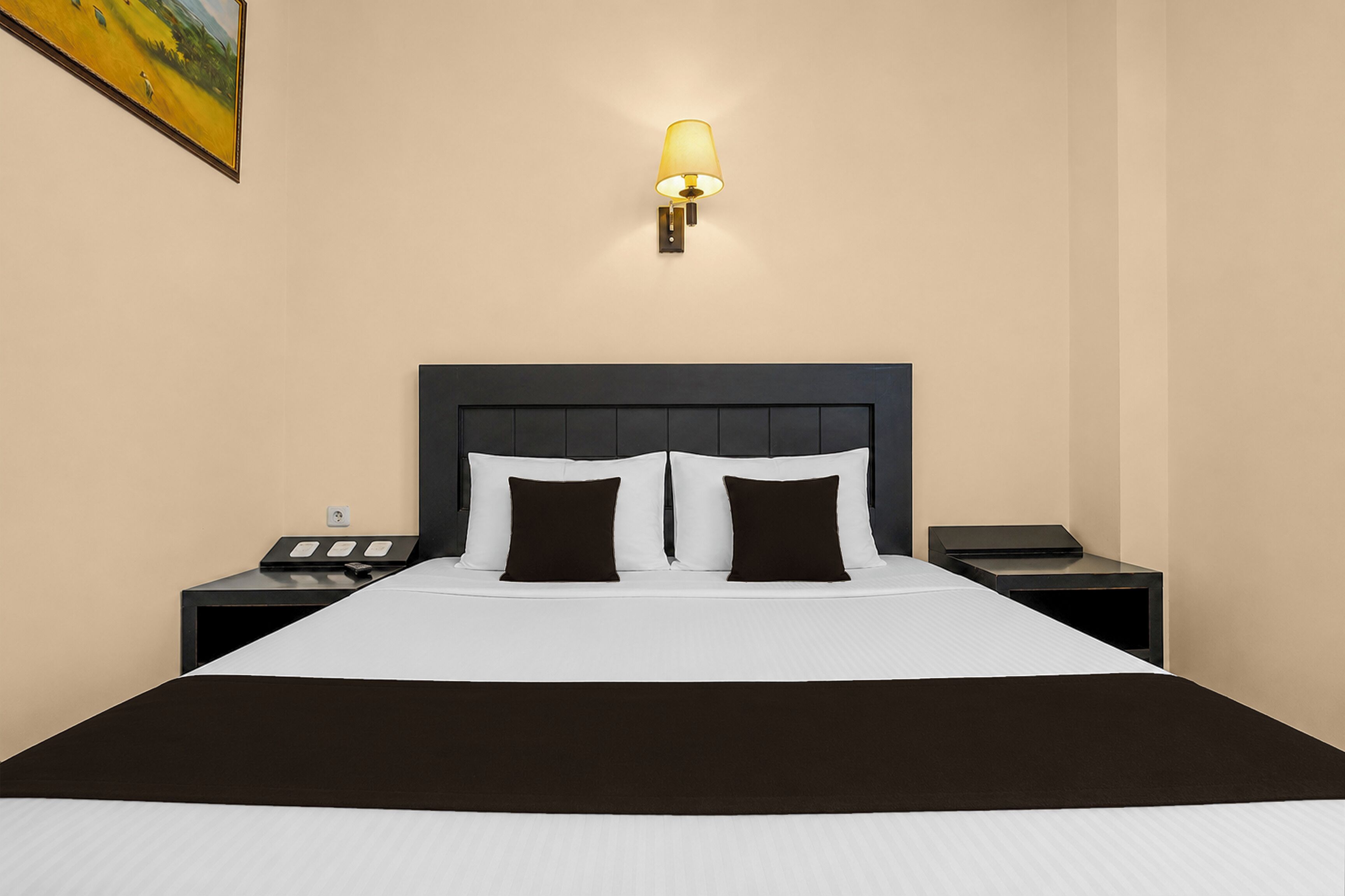 A hotel room with a bed, bedside tables, a lamp, and a painting on the wall.