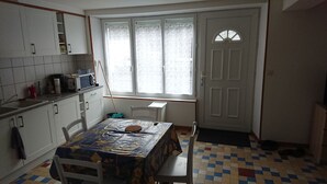Een keuken met witte kastjes, een magnetron en een raam met gezandstraald glas. Er staat een tafel met een kleurrijke tafelkleed en stoelen.