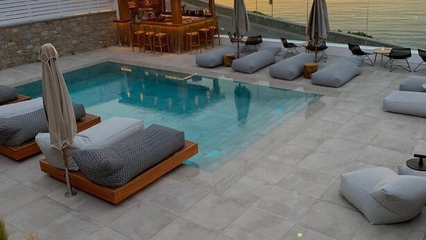 A pool area with lounge chairs, a bar, and a view of the sea at sunset. - Apiro Mykonos (Mykonos)