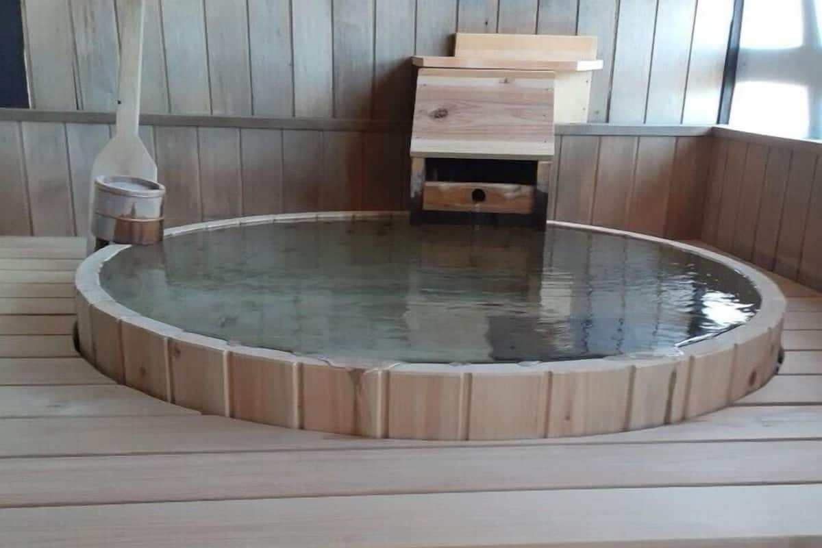 Una bañera de hidromasaje de madera con un banco, un mueble y una pared de madera.