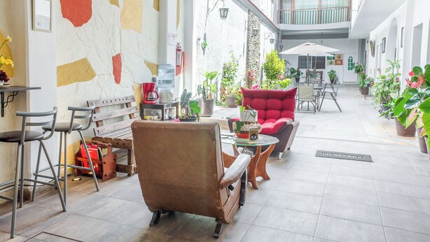 Un vaste espace intérieur doté d’un haut plafond, avec un coin salon central agrémenté d’un fauteuil rouge, de plusieurs tables et de plantes en pot.