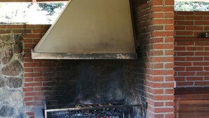 A brick-built outdoor grill with a metal hood, surrounded by stone and brick walls. - Rural tourism homestead JOLE (Rumšiškes)