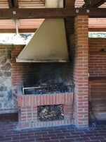 A brick-built outdoor grill with a metal hood, surrounded by stone and brick walls.