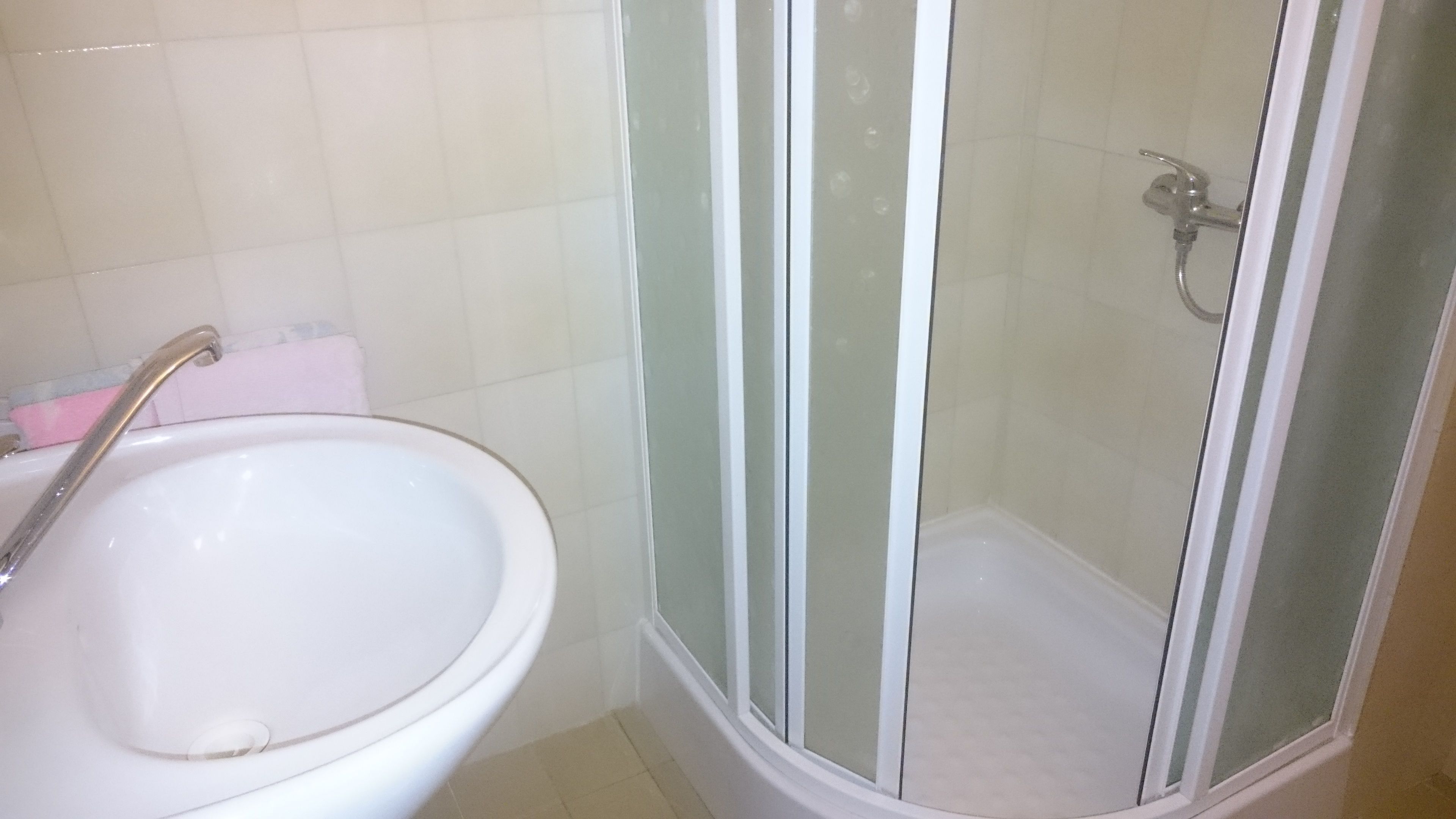 A bathroom with a white sink, a shower with a glass door, and a tiled floor.