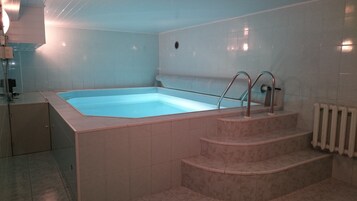 A rectangular hot tub with steps leading into it, surrounded by white tiled walls.
