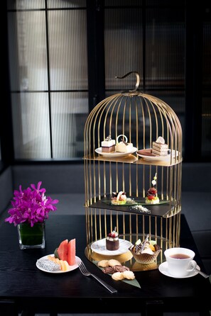 Un expositor de postres de tres niveles en una estructura similar a una jaula, con diversos pasteles y dulces.