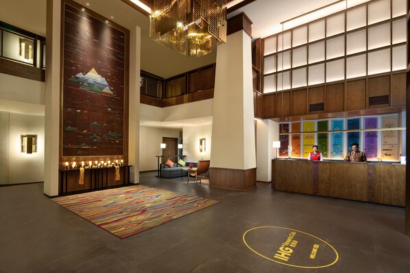 A spacious lobby with a reception desk, a colorful rug, and a large wall mural. - Holiday Inn Batang by IHG (Garze)