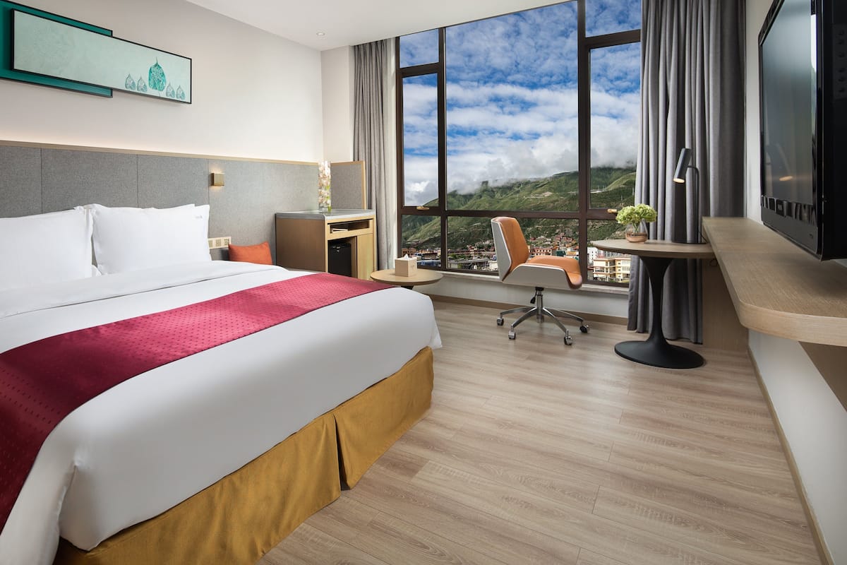 A hotel room with a large bed, a desk, a chair, and a TV.