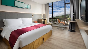 A hotel room with a large bed, a desk, a chair, and a TV.