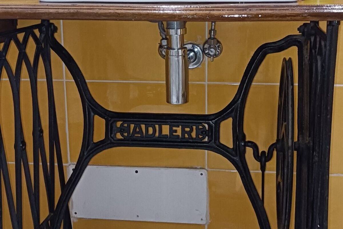 A bathroom with a white sink, yellow tiled walls, and a black metal frame.