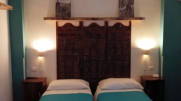 Una habitación con dos camas, ropa de cama color turquesa, un cabecero de madera con detalles artísticos y lámparas de noche.