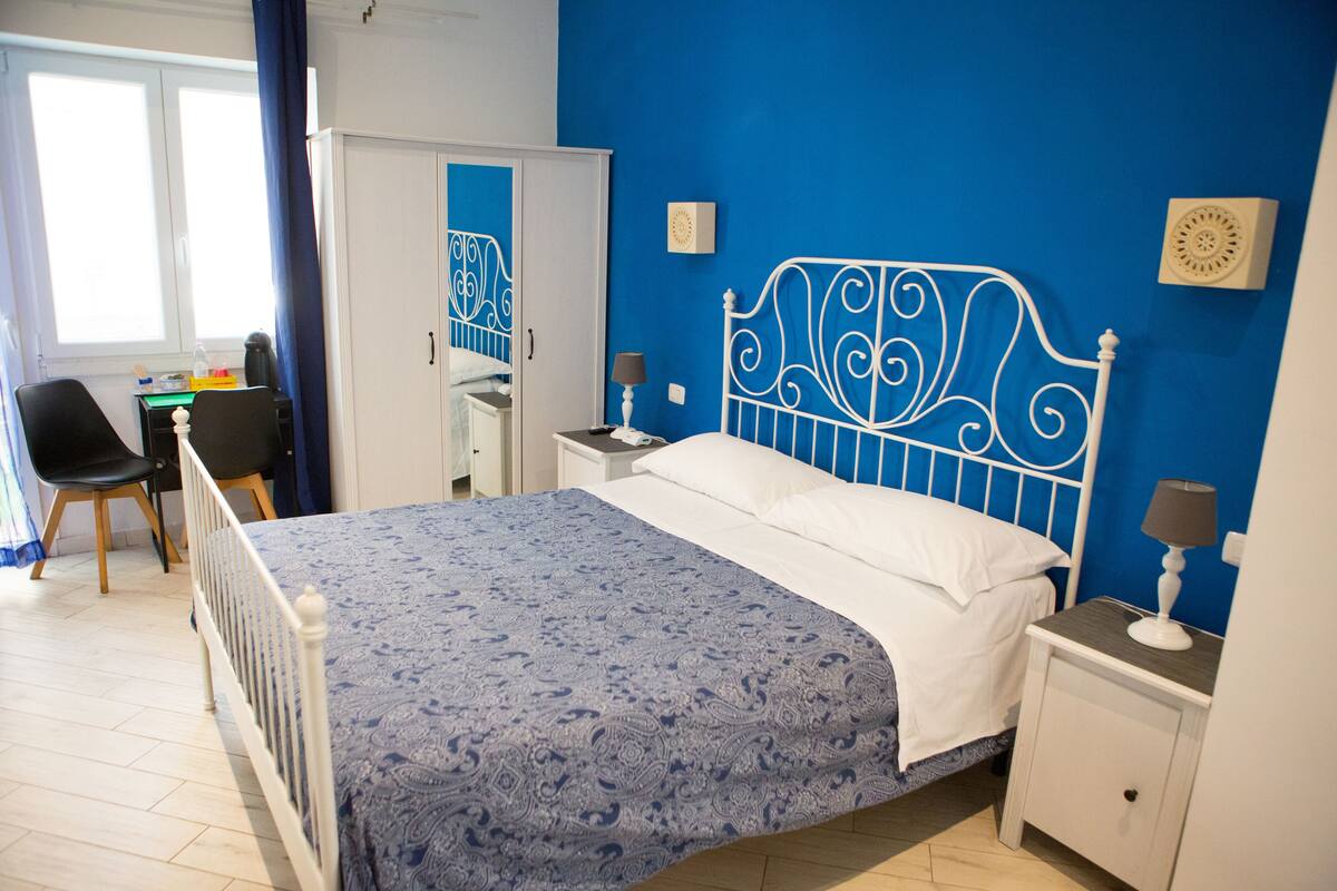 A bedroom with a bed, a nightstand, a desk, and a chair.