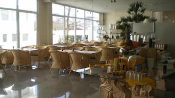 A spacious dining area with wicker chairs and tables, large windows, and a central decorative sculpture.