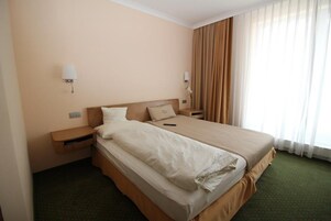 Una habitación de hotel con una cama grande, dos mesitas de noche y un ventanal con cortinas.