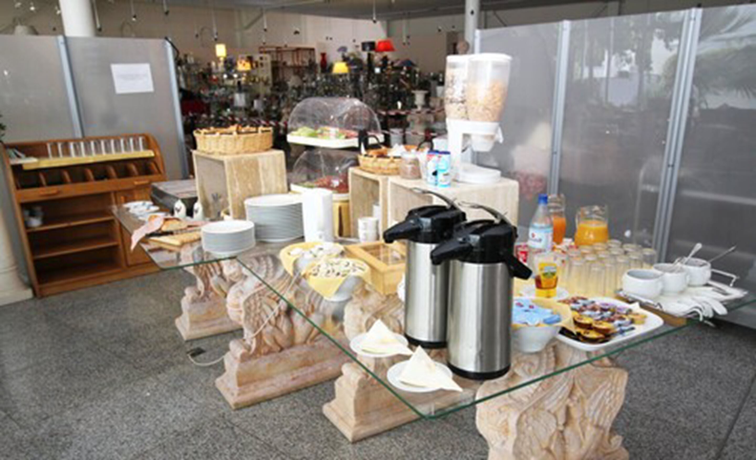 Montaje de bufé con diferentes opciones de comida, una cafetera y una licuadora sobre una mesa de vidrio.