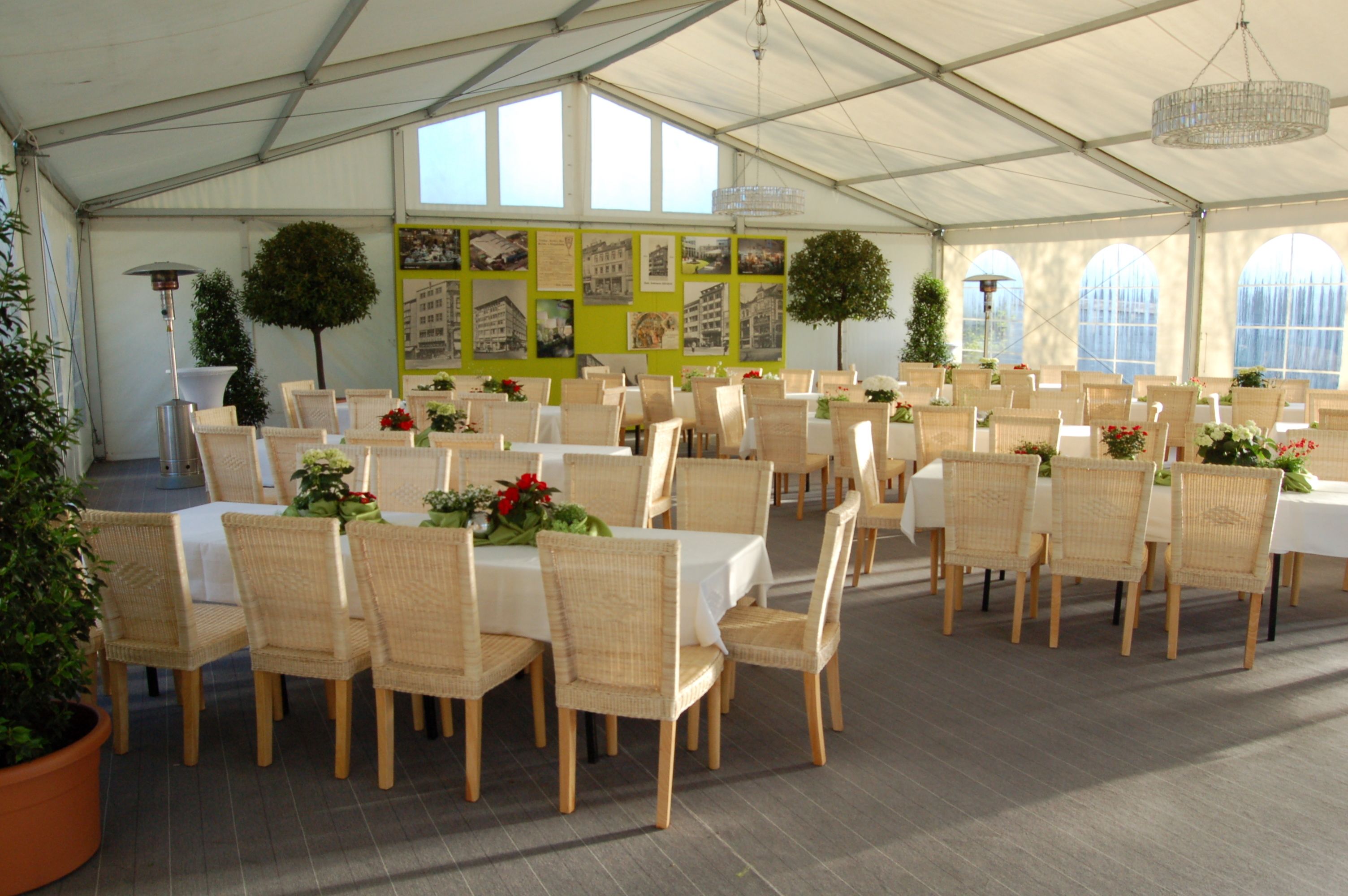 Un área de comedor cubierta con carpas, mesas y sillas de mimbre, decorada con flores y follaje.