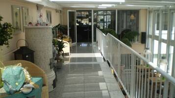 A corridor with a tiled floor, a white railing, and potted plants.