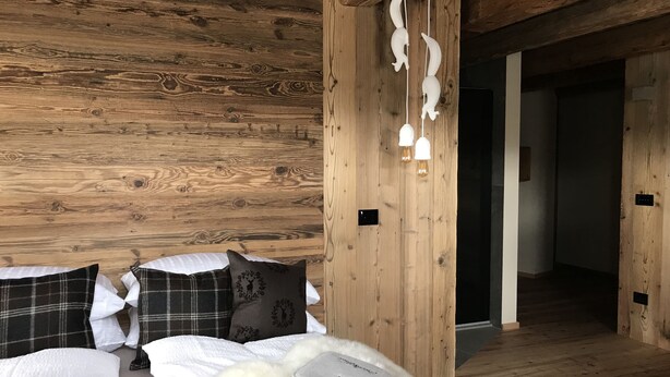 A wooden cabin-style room with a bed, pillows, and a white furry rug. - Grizzly Haus (Ville di Fiemme)