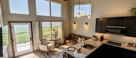 A spacious living area with a large window, a cozy seating area, and a kitchen with modern appliances.