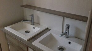 A bathroom with two white sinks, a mirror above, and a wooden shelf. - 4/6-person CLIMATIZED WOODEN CHALET, near Algajola beach, countryside & village views (Pigna)