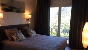 Un dormitorio con una cama grande, dos lámparas de noche, vistas a un balcón y un cuadro en la pared.
