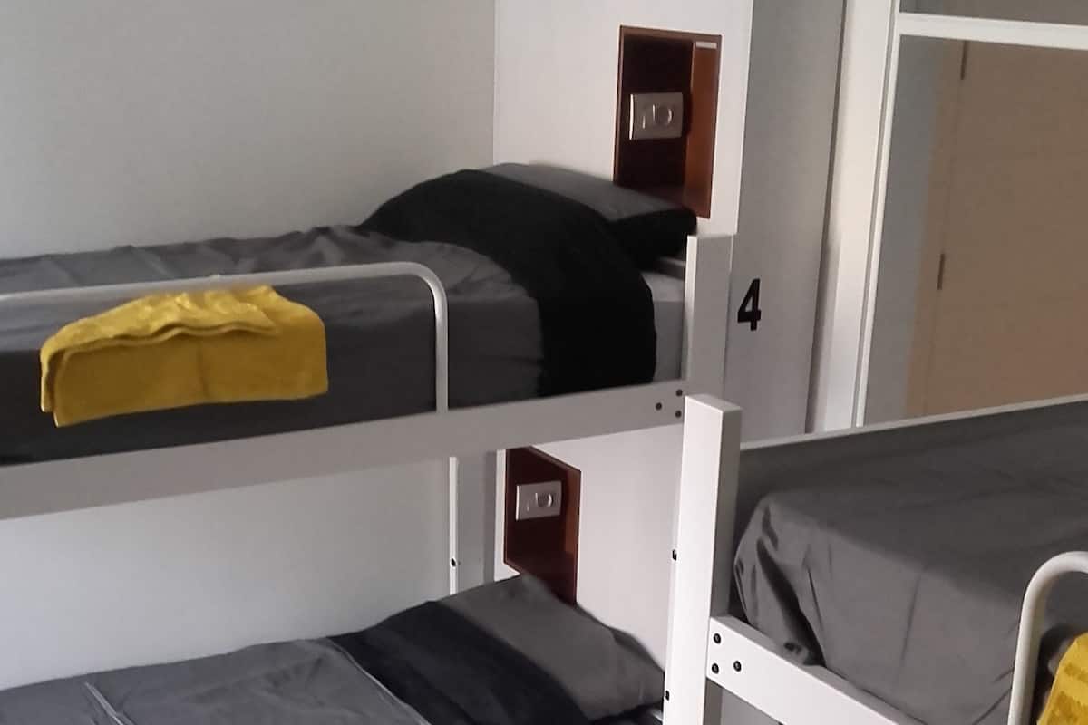A dormitory room with bunk beds, numbered storage compartments, and a small desk with a chair.
