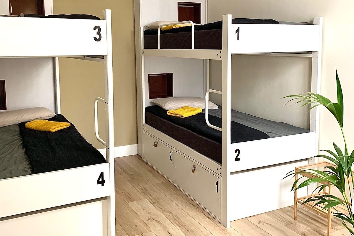 A dormitory room with bunk beds numbered 1 to 4, wooden flooring, and a hanging light fixture.