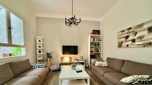Una sala de estar con dos sofás, una mesa de centro, un televisor, una estantería y una araña.