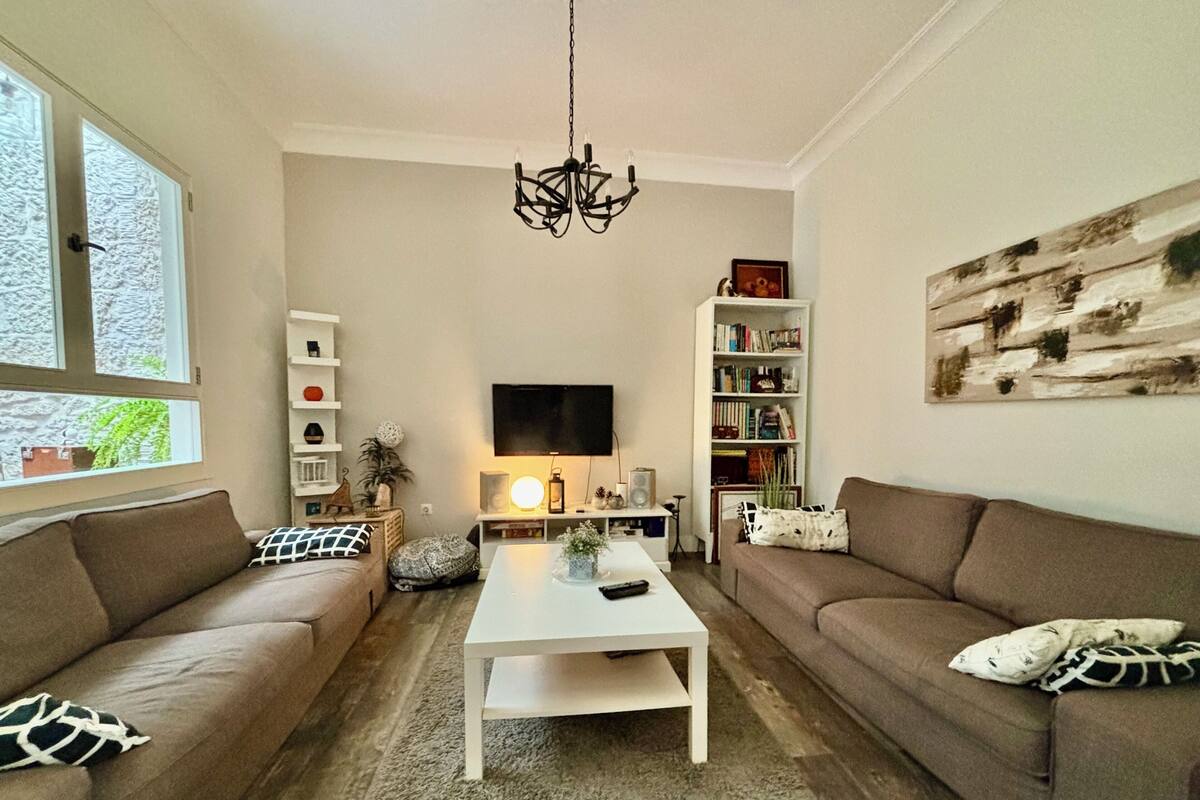 A living room with two sofas, a coffee table, a TV, a bookshelf, and a chandelier.