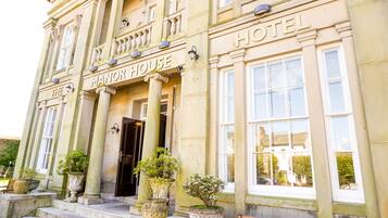 Welcome to the Manor House Hotel, featuring a stately exterior with classical columns and decorative moldings.