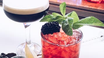 Un cóctel con hielo y una mora como adorno, una copa de martini y un pequeño recipiente con bayas.